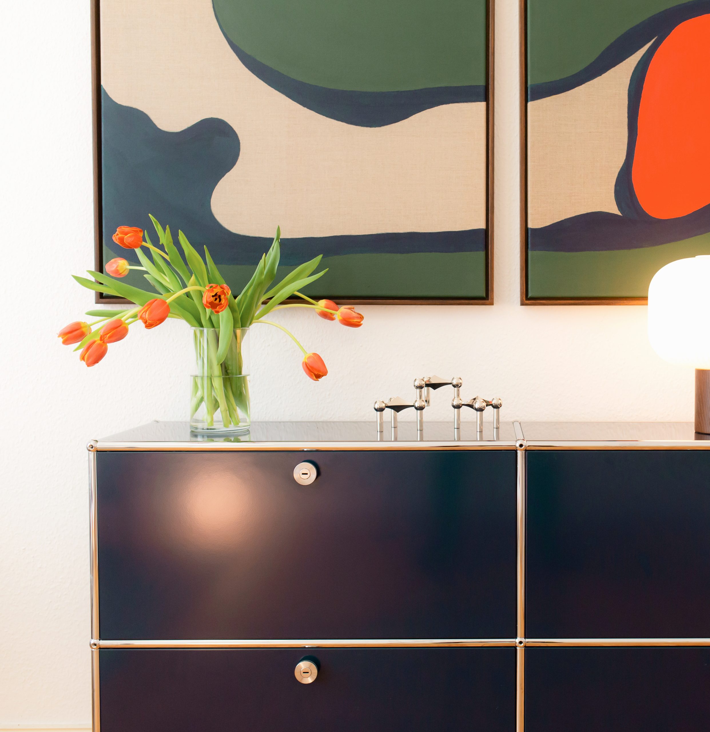 Einblick in den Praxisraum der Psychotherapeutin Paulina Wilkens in Berlin: Abstraktes Wandbild und Blumen auf einem Regal bei warmer Beleuchtung.